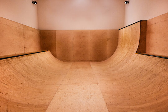 An indoor skateboard sports ramp / halfpipe lit by spotlights with no people, wooden texture and wooden & plaster walls, symmetrical and minimal composition. underground skate social / competition