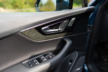Cropped view of driver's side car door with knob and switches on control panel. Window push buttons, automotive lock and design specifications regarding safety and functionality