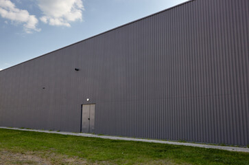 Fototapeta na wymiar Corrugated steel warehouse or factory industrial building against blue sky. Architecture. Metal texture