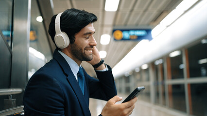 Smart business man listening music by headphone while waiting train at train station with blurring...