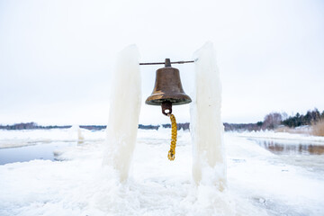 Rustic bell hanging between ice pillars at a winter swimming location with a frozen lake in the...