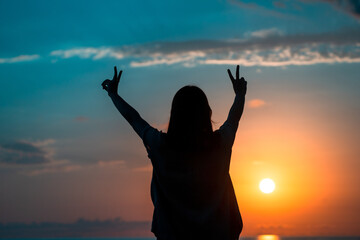 A girl makes a v sign with her hands as a sign of victory at sunset