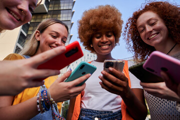 Low angle view of a group of multiracial young women friends using smartphones addicted to...