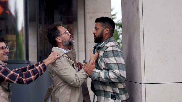 Angry man is aggressive, have conflict with young man, holding him by shirt, screaming, threatening him. Friend helping to end fight.
