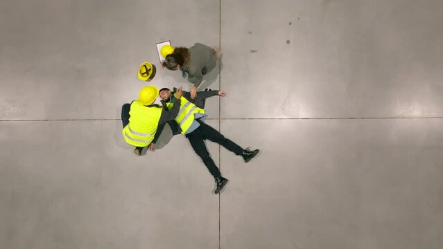 Colleagues giving first aid to unconscious worker after accident at work in warehouse, factory. Calling the ambulance. Concept of occupational safety and health in workplace.