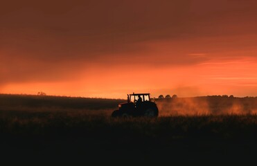 Fototapeta premium an tractor is driving in the field at sunset