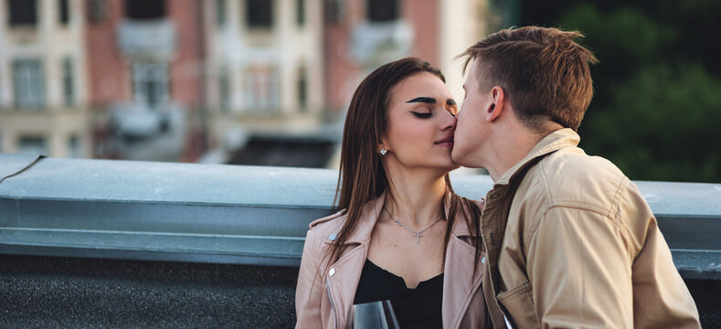 Beautiful young loving couple on a surprise romantic date on a roof top. Picturesque view, skyscrapers on background. Wine, candles, kisses on holiday Saint Valentine's Day celebration outdoors