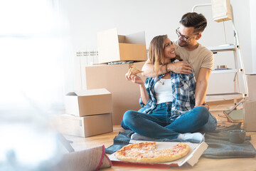 Loving smiling couple embracing and looking at each other while sitting on floor and eating pizza...