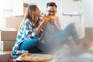 Half blurred photo of loving heterosexual couple eating pizza for breakfast in new apartment. - obrazy, fototapety, plakaty