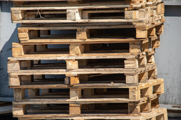 Used wooden pallets stacked along a wall in a warehouse lot.