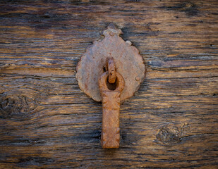 Ancient door knocker on wooden door .