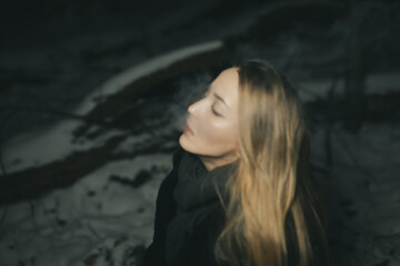 Young blond Woman with black dress in the wood at an snowstorm in deep winter at berlin forrest