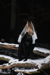 Young blond Woman with black dress in the wood at an snowstorm in deep winter at berlin forrest