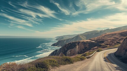  a scenic view of the ocean and mountains from a high point of view of a road on the side of a cliff, with a blue sky and white cloud filled with wispy wispy wispy clouds. - obrazy, fototapety, plakaty