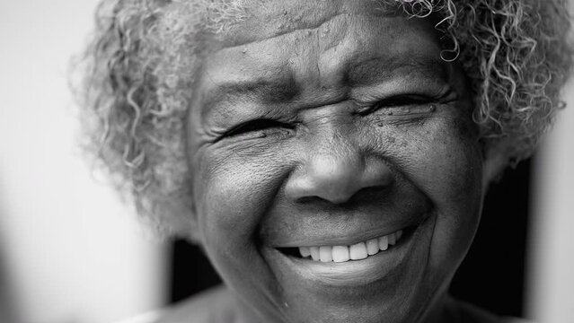 One happy black senior woman in 80s in black and white. Monochromatic portrait of wise older African American lady smiling at camera showing old age and wisdom