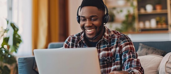 A happy African American man is using a laptop at home, smiling while having an online meeting with a headset.