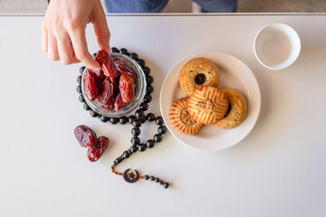 hand holding eid sweets and dates on white table with rosary and cup of coffee