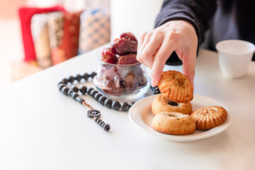 hand holding eid sweets and dates on white table with rosary and cup of coffee