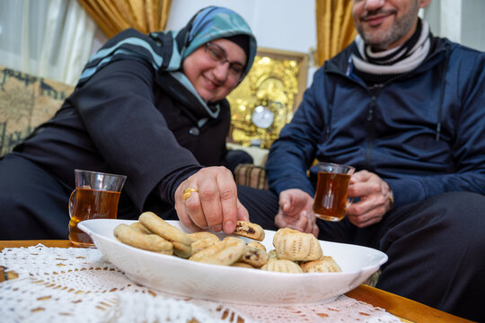Female enjoy eating eid kahk while drinking tea with smile on face