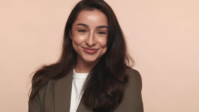 Smiling Shy Armenian businesswoman showcases professionalism in a stylish blazer against a warm beige backdrop in a studio setup