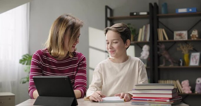 Happy family. Mother helping son doing homework at home desk. Mother and son together studying online with digital tablet. Children remote education