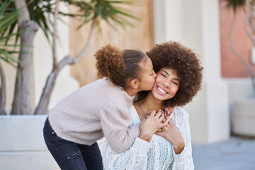 Girl with afro hair looking at the camera as her sister hugs and kisses her. family relationships