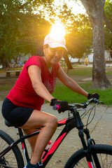 Hispanic Latin brunette woman on bicycle and with sun in the background in Neiva park - Huila -...