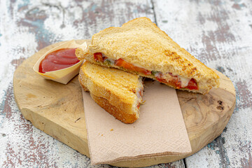 Toasted sandwich with mozzarella cheese, pesto and tomato served with ketchup sauce on the side, The croque-monsieur is a hot sandwich in wood plank on wooden table.
