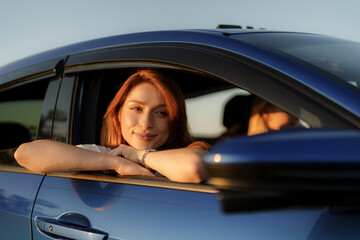 Young woman enjoying a serene moment leaning from a car during a sunset, depicting travel and freedom