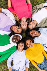 High angle view. Portrait of diverse happy women looking at camera lying together on grass at city...