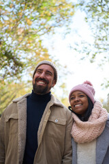 Vertical Portrait of beautiful multi-ethnic happy young couple outdoor in love smiling looking around in a street in christmas time. People dressed in winter clothes having fun together. 