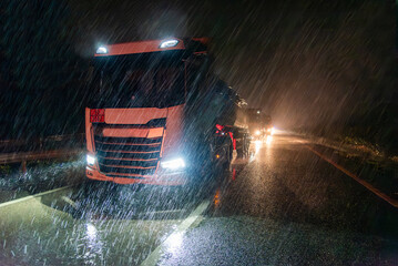 Tanker truck with dangerous goods license plate on the highway at night on a day of heavy rain.
