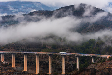 Truck with a refrigerated semi-trailer driving over a bridge and a mountain landscape with low...