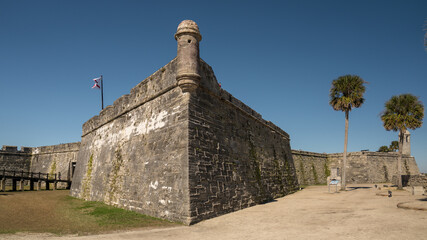 Castillo de San Marcos National Monument in St. Augustine with a flag and palm trees against a blue sky.