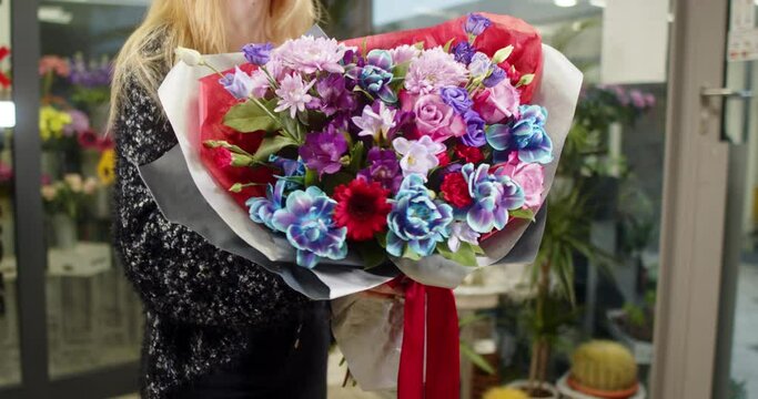 Girl shows a bouquet of blue rose, Alstromerie, Eustoma, Fresie, Chrysanthemy in a flower store