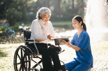 Elderly asian senior woman on wheelchair with Asian careful caregiver and encourage patient, walking in garden. with care from a caregiver. and senior health insurance