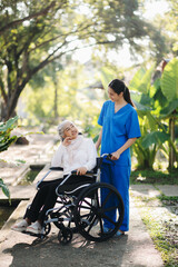 Elderly asian senior woman on wheelchair with Asian careful caregiver and encourage patient, walking in garden. with care from a caregiver. and senior health insurance