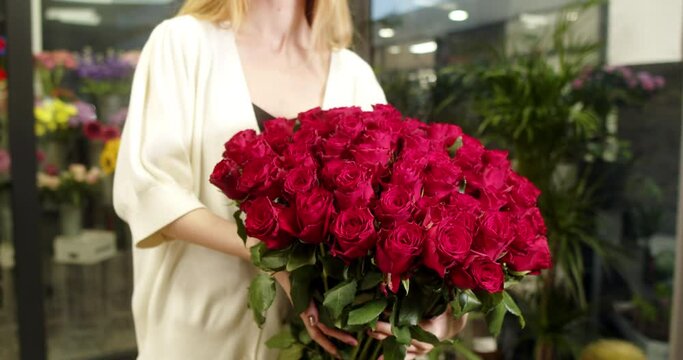 A girl in a flower store holds and shows a bouquet of medium-sized red roses 101 pieces