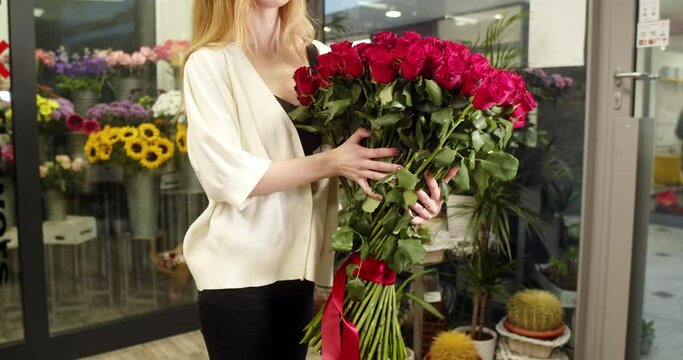 A girl in a flower store holds and shows a bouquet of medium-sized red roses 101 pieces