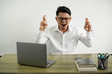 angry young asian businessman in a workplace with finger crossing, wearing white shirt with glasses isolated