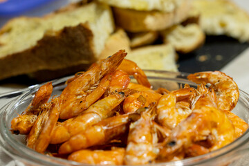 Grilled shrimp with garlic in a glass bowl with toasted bread on the background.