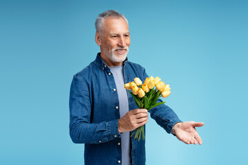 Portrait of smiling attractive senior man giving yellow spring tulips. Concept of March 8, dating