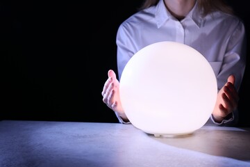 Businesswoman using glowing crystal ball to predict future at table in darkness, closeup. Space for...