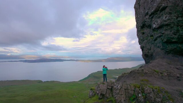 AERIAL: Smiling tourist admires the views around her at the Old Man Of Storr. Young woman is impressed by the picturesque landscape and takes photos with her phone. Iconic landmark at the Isle of Skye