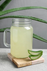 Tasty aloe juice in mason jar and cut fresh leaves on light grey table