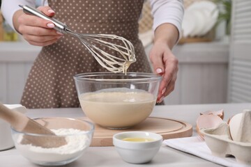 Woman making dough with whisk in bowl at table, closeup