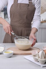 Woman making dough with whisk in bowl at table, closeup