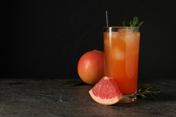 Tasty grapefruit drink with ice and mint in glass on dark textured table. Space for text