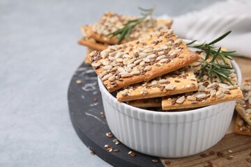 Cereal crackers with flax, sunflower, sesame seeds and rosemary in bowl on grey table, closeup. Space for text