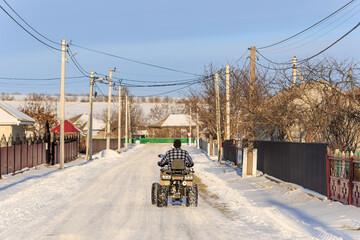 Naklejka premium A man on an ATV rides through the village in winter. Background with selective focus and copy space